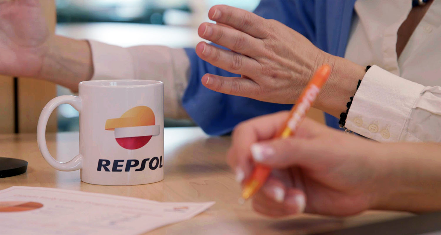 Vista de una mesa de reuniones con una taza blanca con el logo de Repsol 