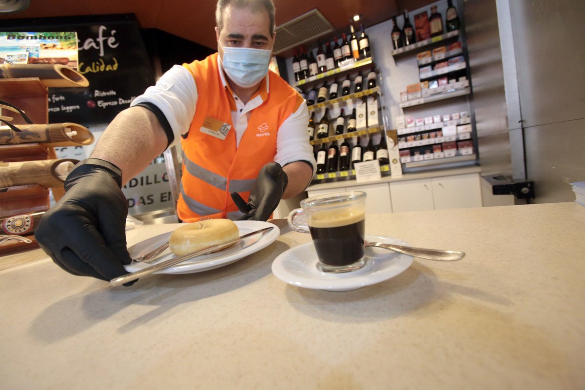Un empleado de una estación de servicio de Repsol con mascarilla sirve un café