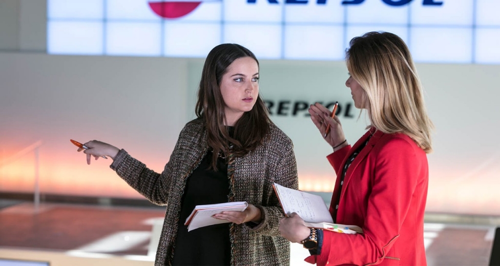 Two women talking in front of a Repsol logo. Solid relationships