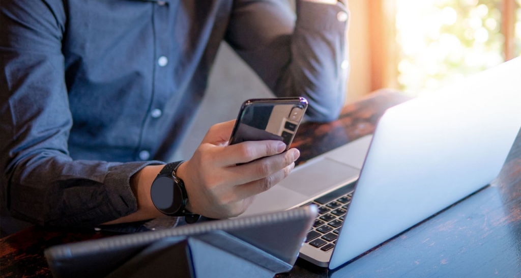 A hand holds a mobile. A glass table with a laptop