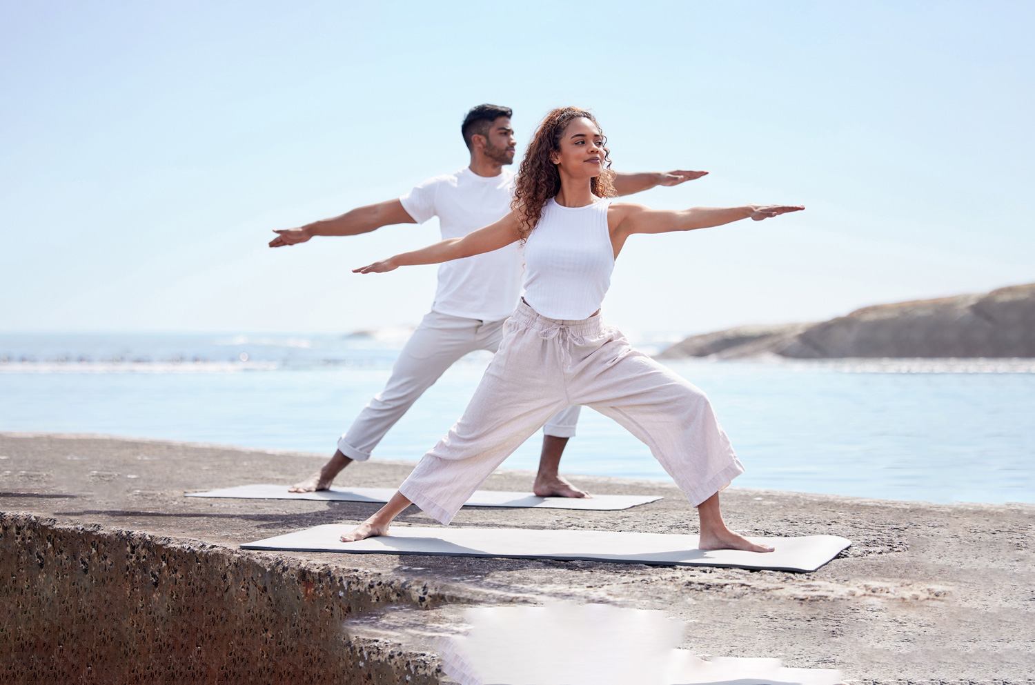 Two people doing yoga in front of the sea