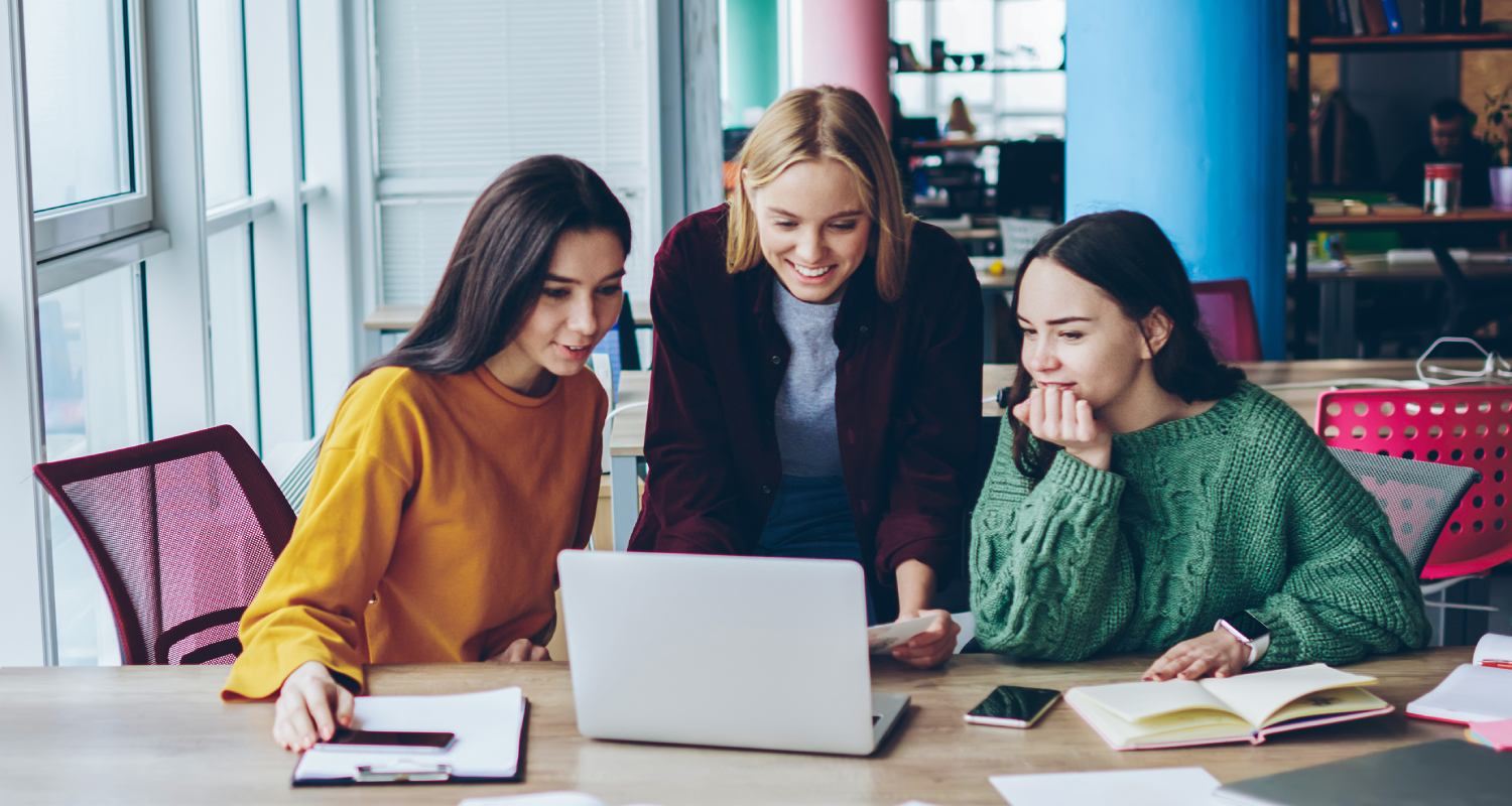 Three women standing In front of a laptop