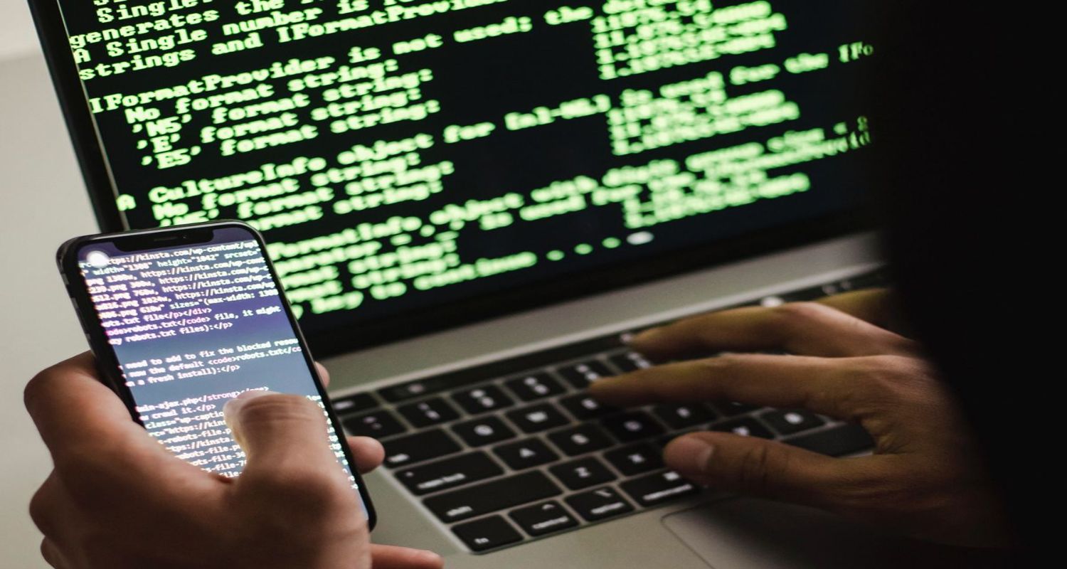 A person holding a smartphone in one hand while typing on a laptop