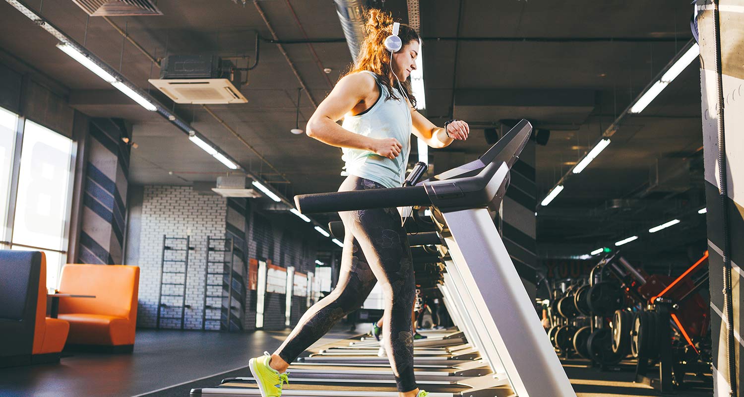Una mujer corriendo en una cinta de un gimnasio mientras escucha música a través de unos auriculares