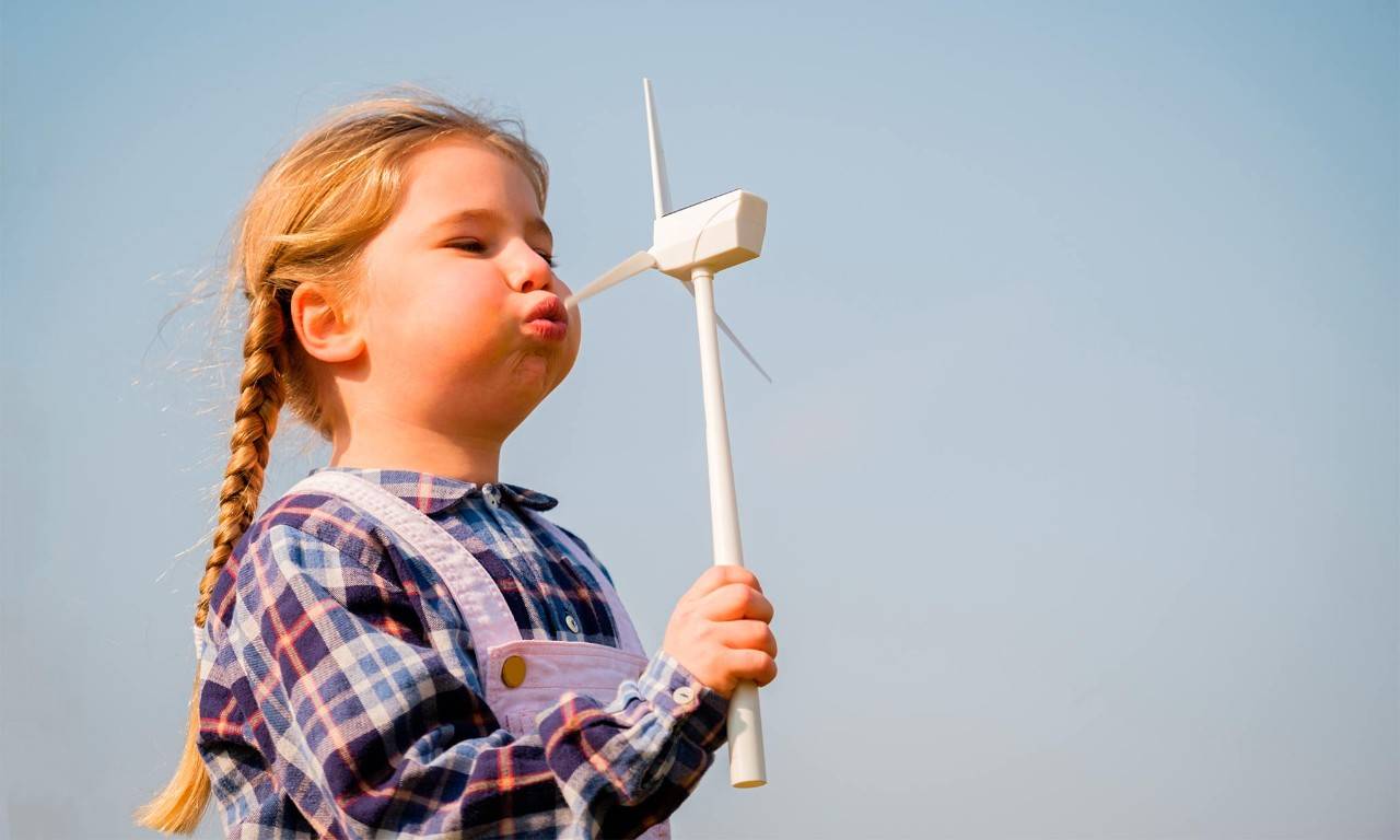 Una niña sopla un molino de aire representando energía sostenible