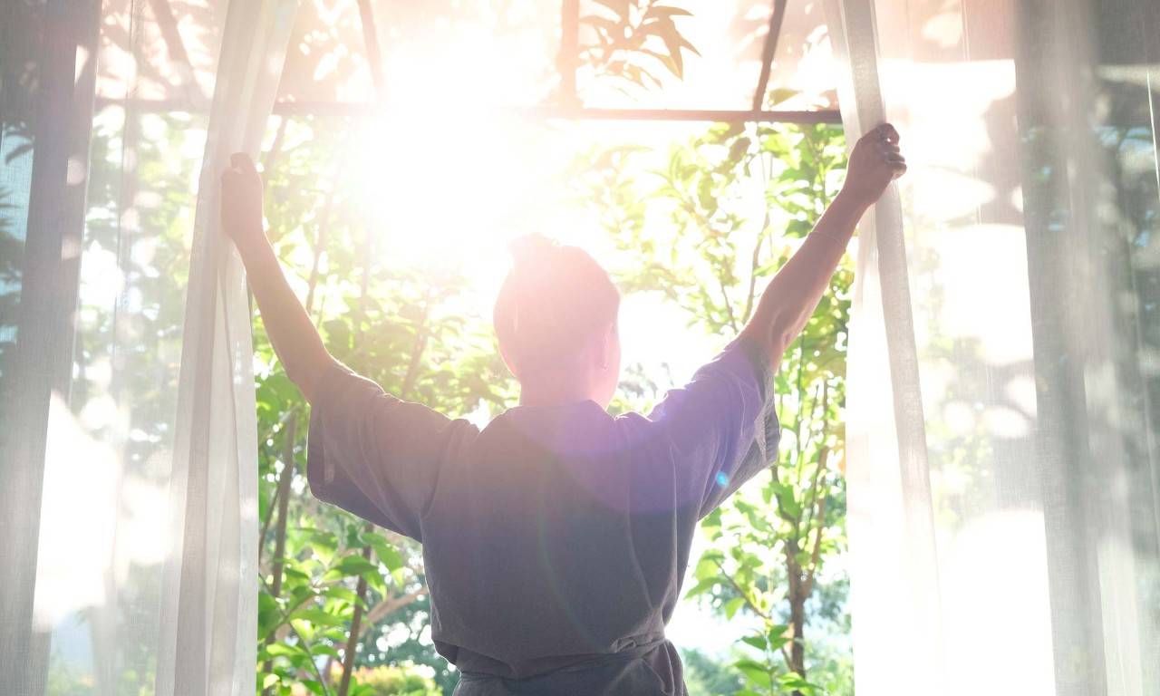 Una mujer abre la ventana para que la luz solar entre