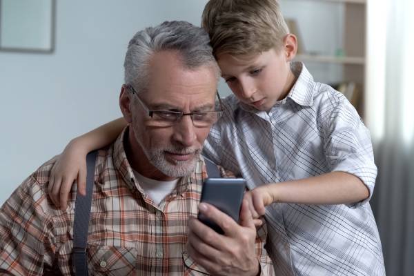 child teaching his grandfather how to use his mobile phone