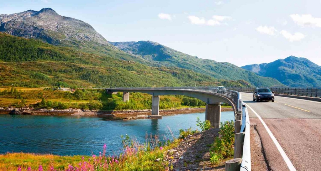 A car driving on a road surrounded by mountains and a river