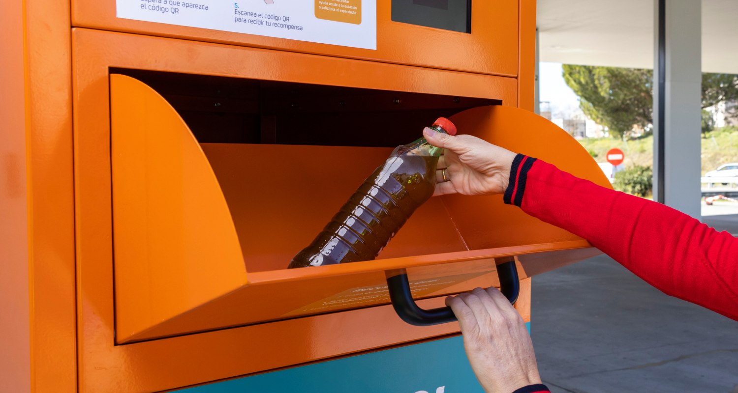 Someone placing a bottle of used cooking oil into a collection container.