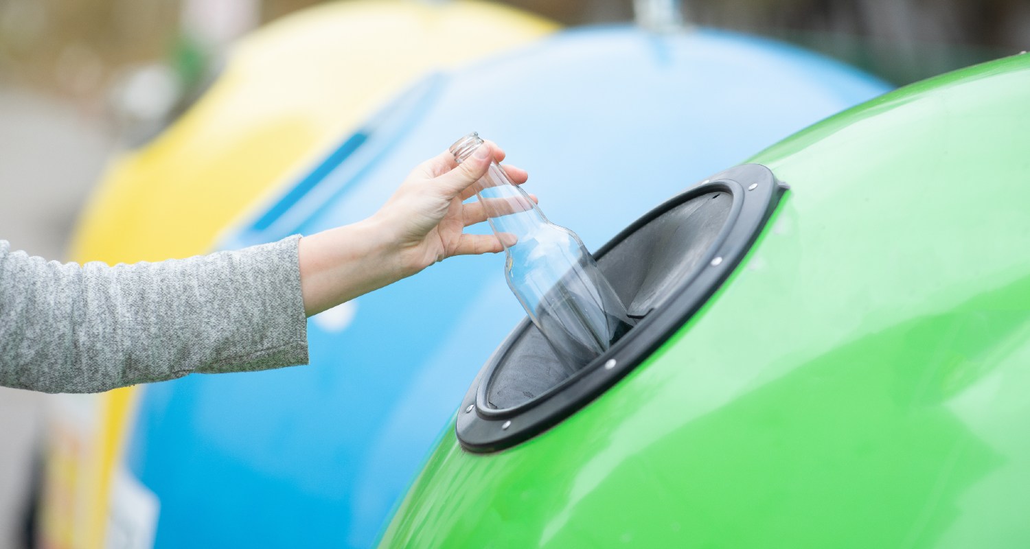 A person throwing a glass bottle in a recycling bin