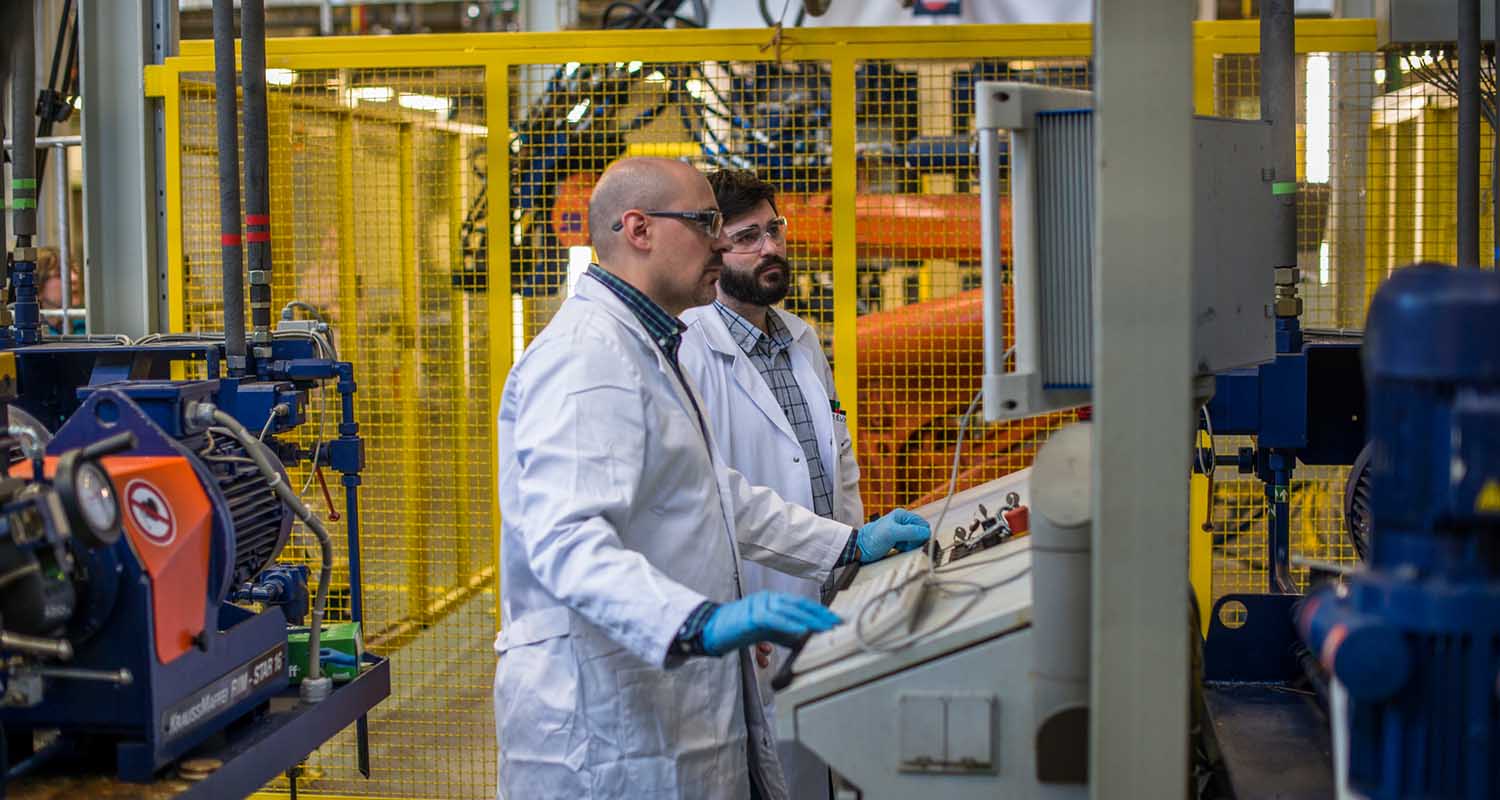 Two employees in white coats and safety goggles at a computer