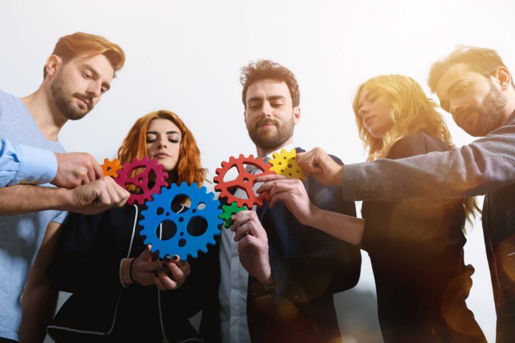 Several people holding colored gears simulating teamwork