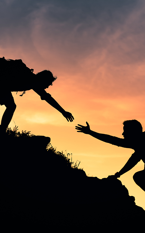 una persona ayuda a otra a subir una montaña
