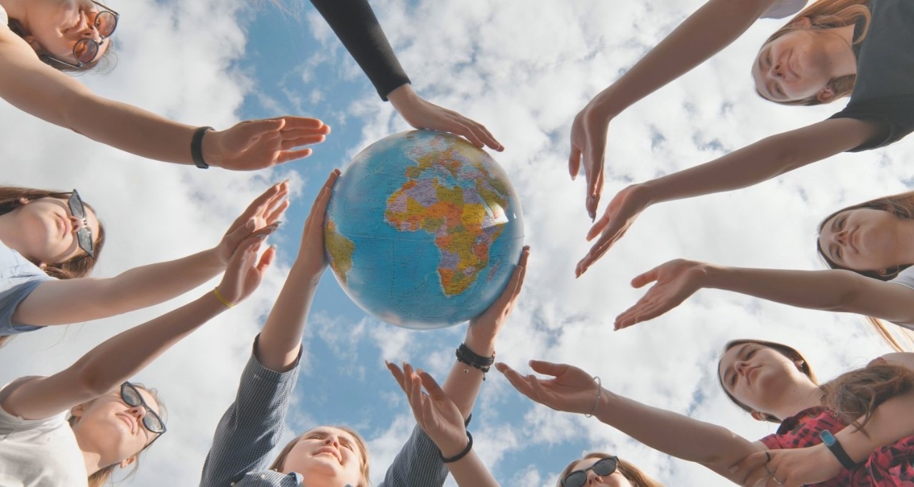 Un grupo de jovenes extienden sus manos para tocar un globo terráqueo