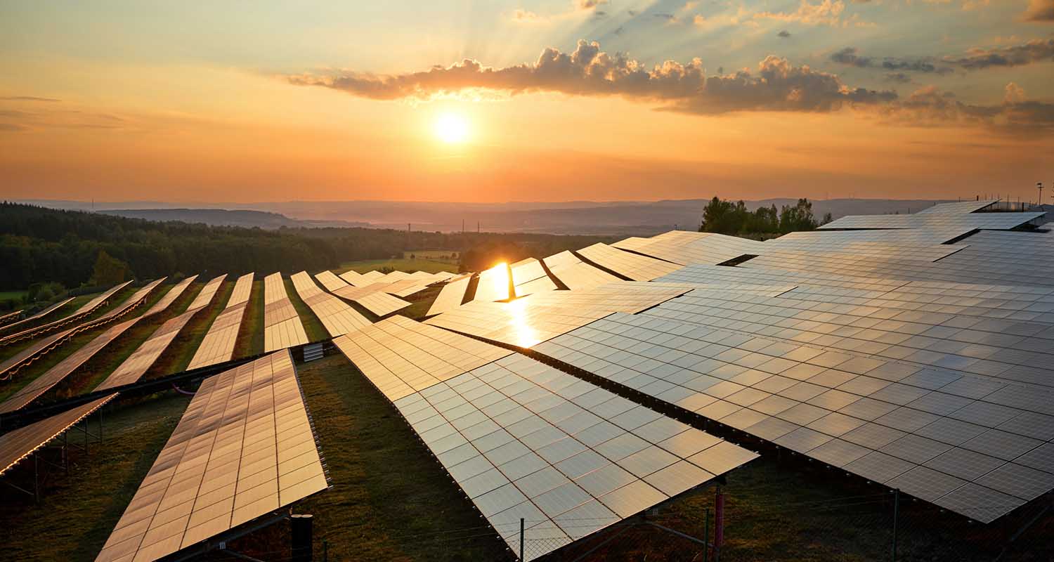 Solar panels in a field at dusk and the sun shining on them