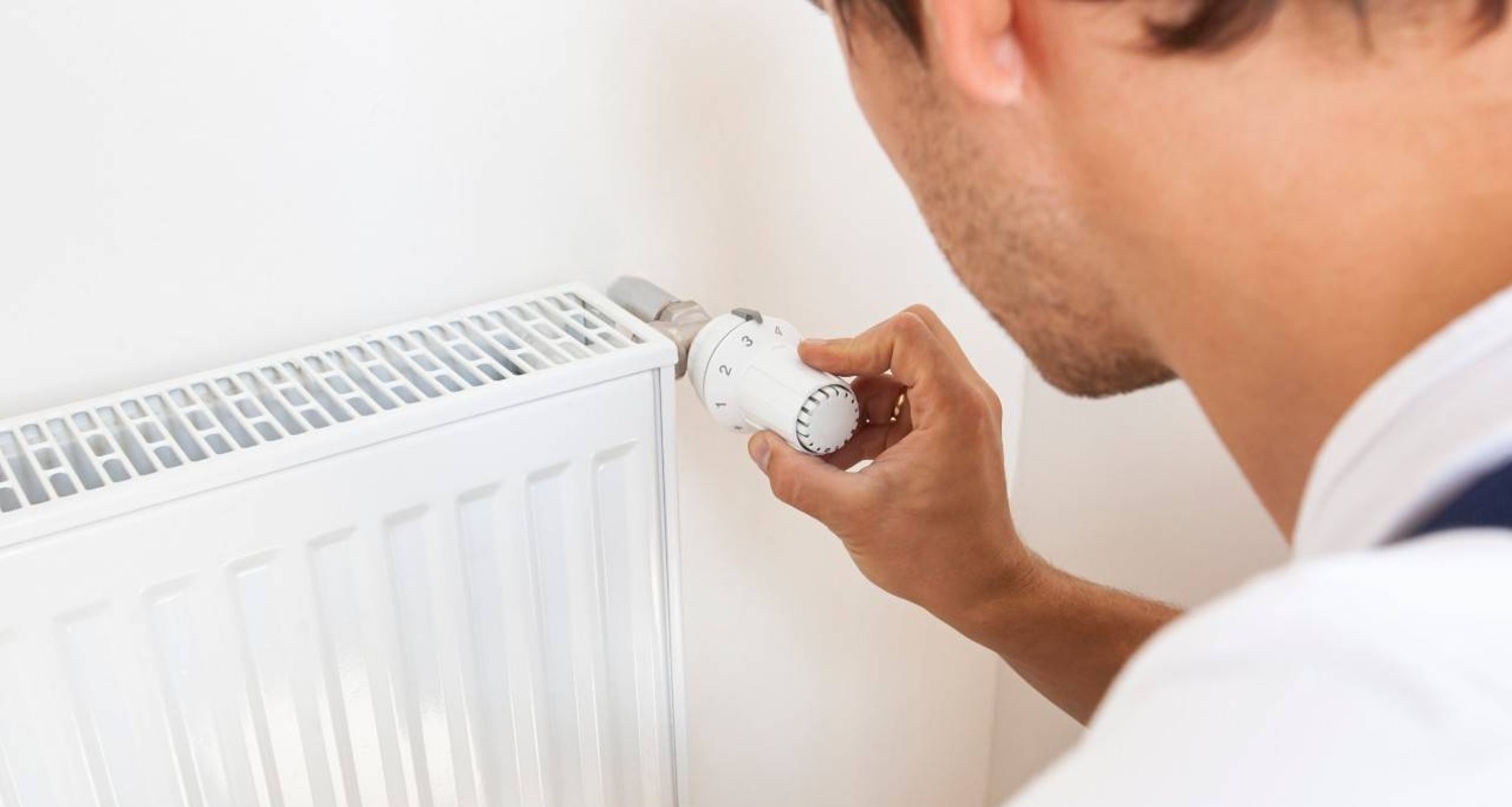 un hombre ajustando la temperatura de un radiador con un termostato inteligente