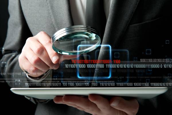 man using magnifying glass to observe data on a tablet