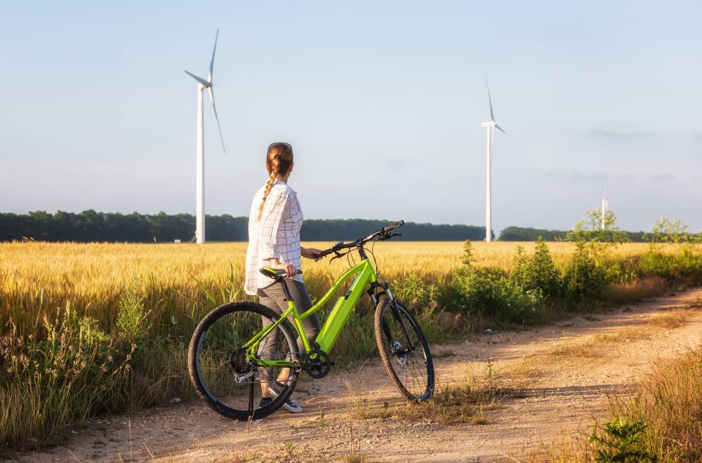 woman walking with her bike through a field of grains with wind turbines in background