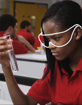 A girl wearing safety goggles examines the contents of a test tube