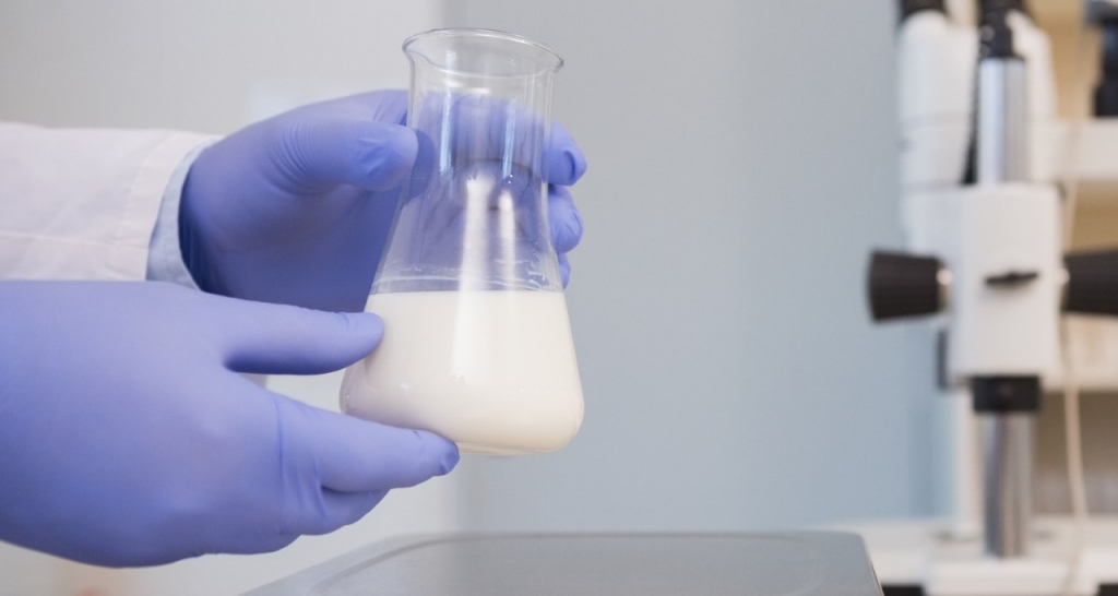 Some hands hold a flask with a white liquid