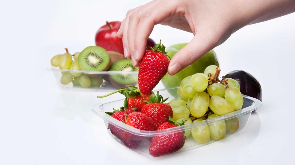 Detalle de una mano tomando una fruta de un recipiente de plástico 