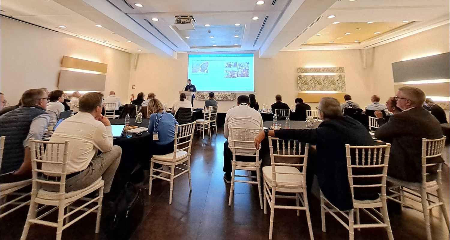 Sala con personas sentadas en sillas alrededor de mesa atendiendo a una presentación