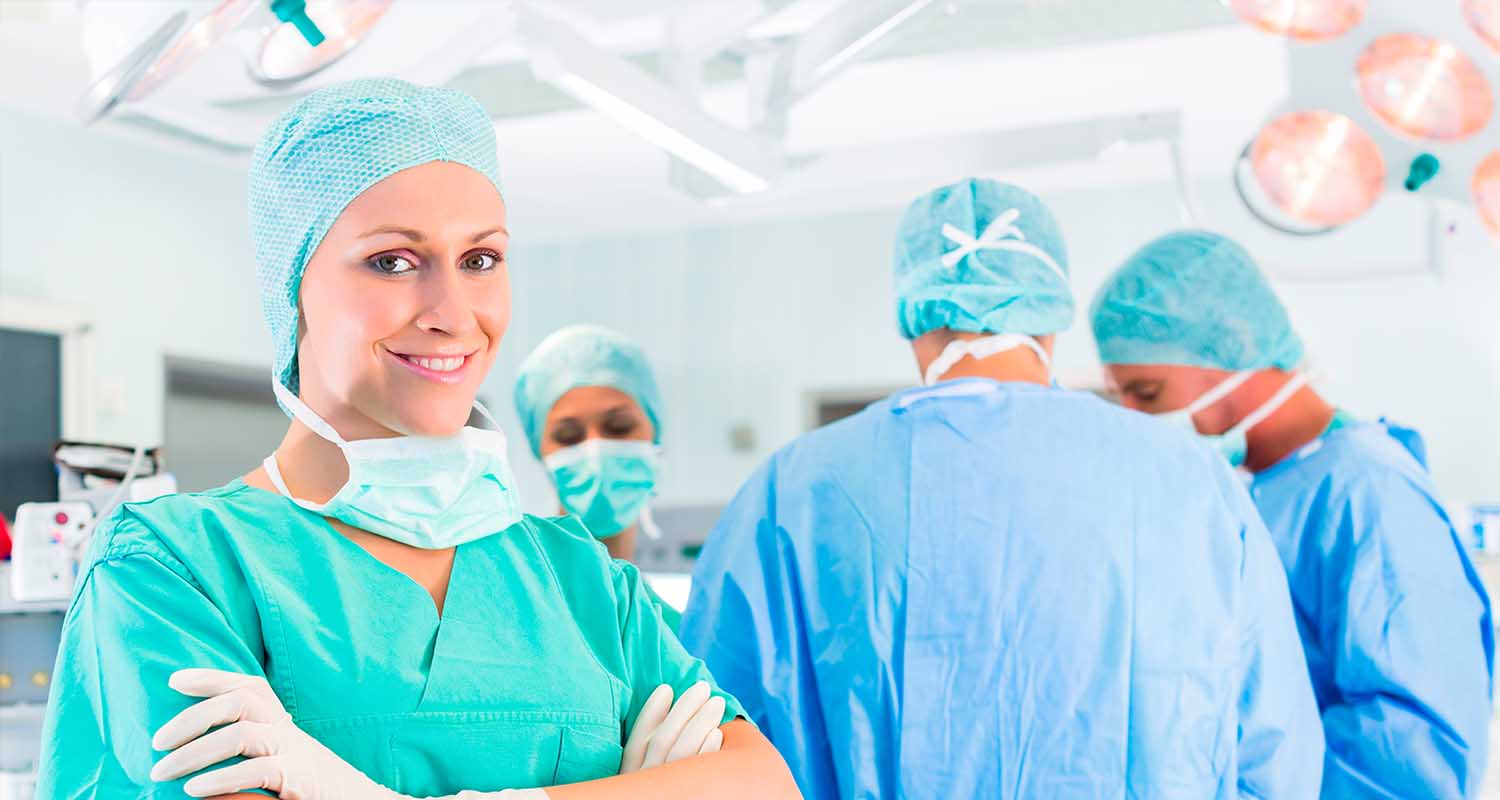 Mujer con ropa de quirófano posa en primer plano delante de un grupo de médicos