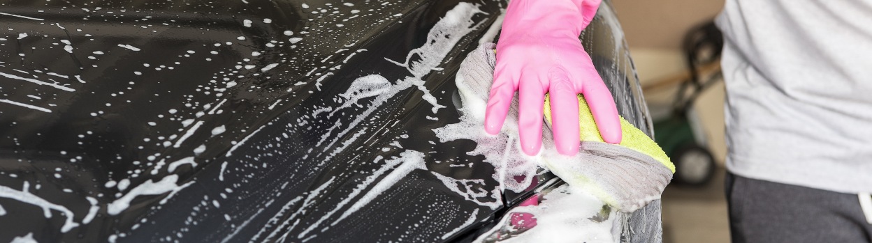 A person washes their car with soap and a cloth