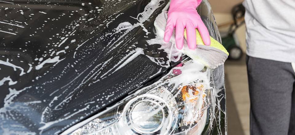 Una persona limpa su coche con un trapo y jabón 