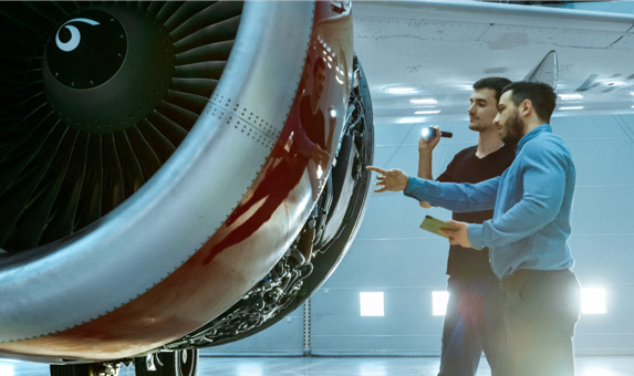 Two people check the inside of an airplane turbine with a flashlight