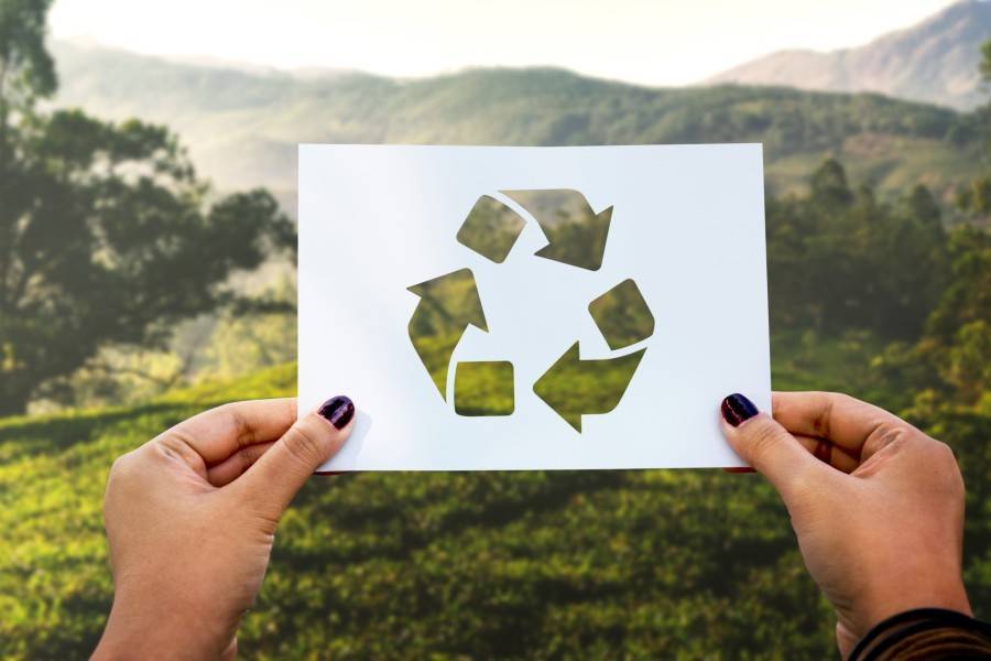 Hands holding the recycling symbol against a green landscape