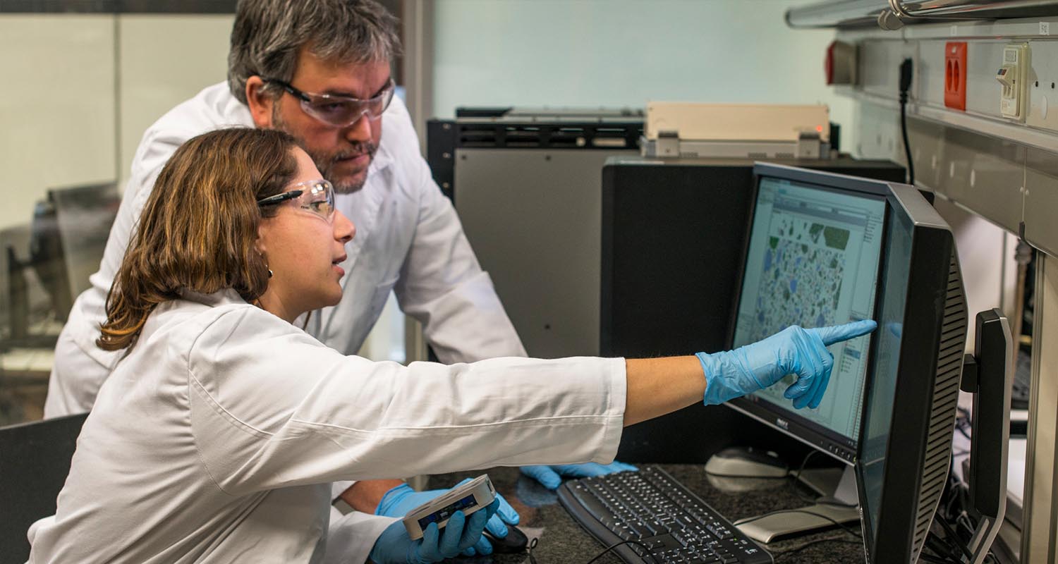 A female researcher points to a computer and a male researcher listens to her