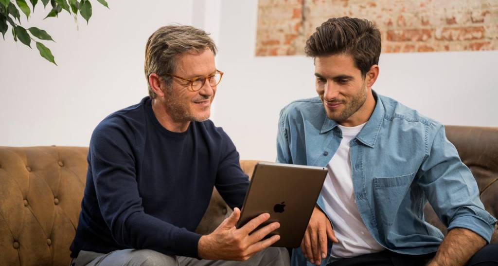 Two men sitting on a couch looking at a tablet