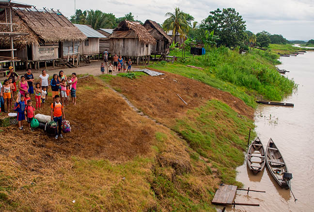 Repsol en el mundoPerú. Grupo de personas en un poblado de casas de madera y paja y el rio amazonas a la derecha con dos barcas de madera