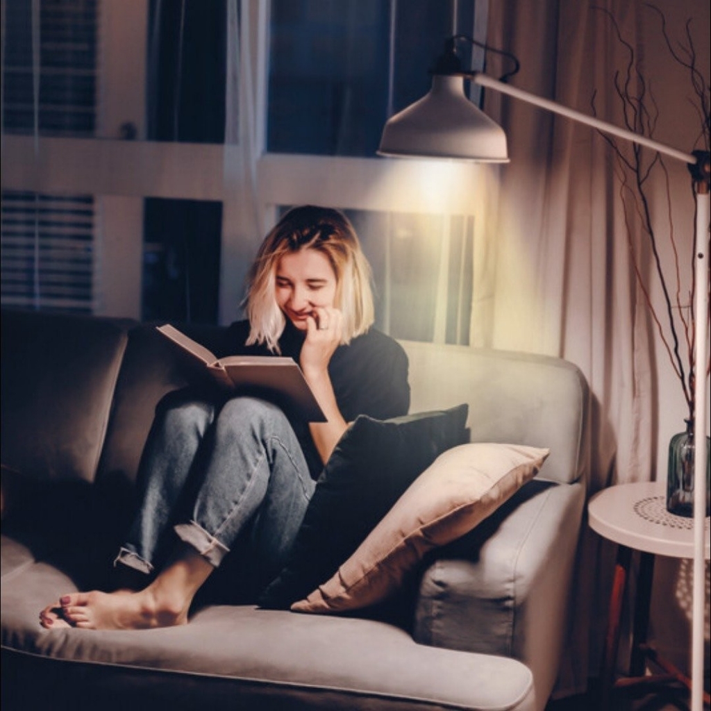Young woman on the couch reading with a lamp next to her