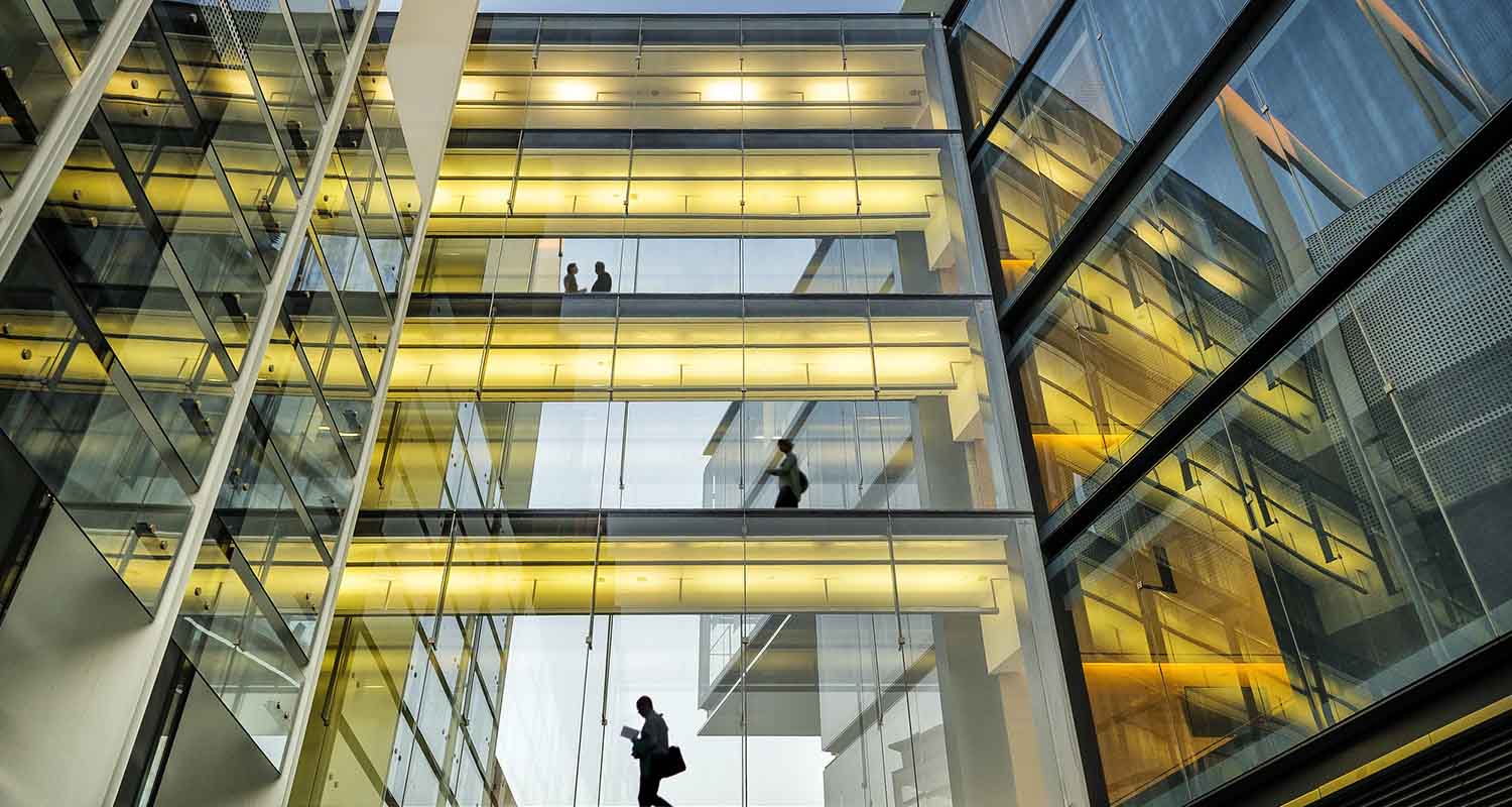 Vista de la fachada acristalada de un edificio con gente dentro de una oficina