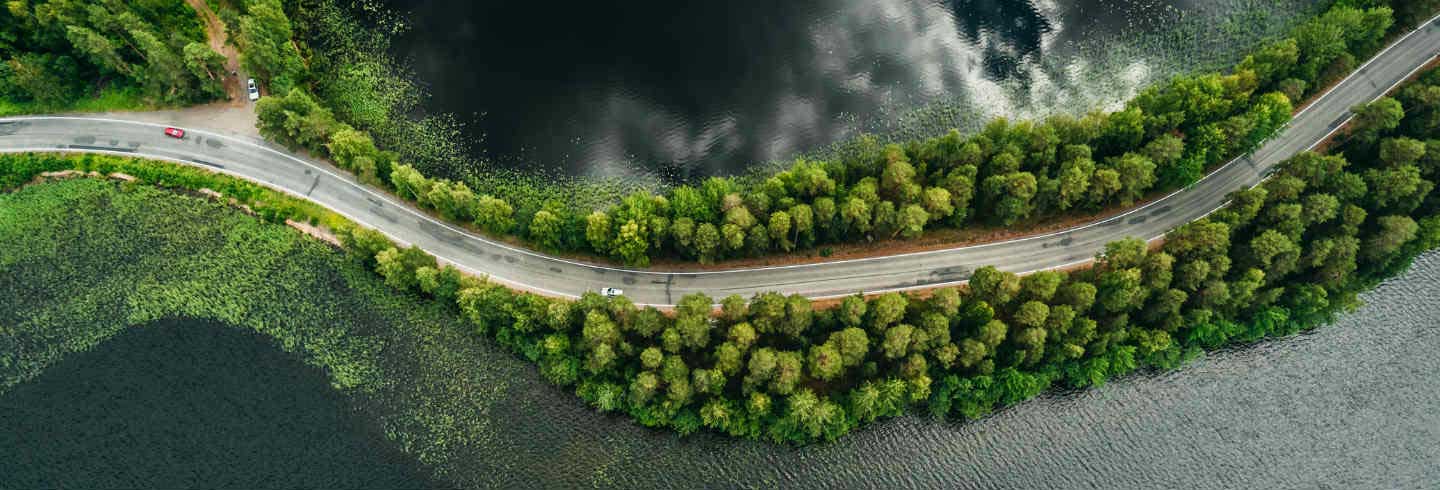 A car drives along a road between a forest and a lake