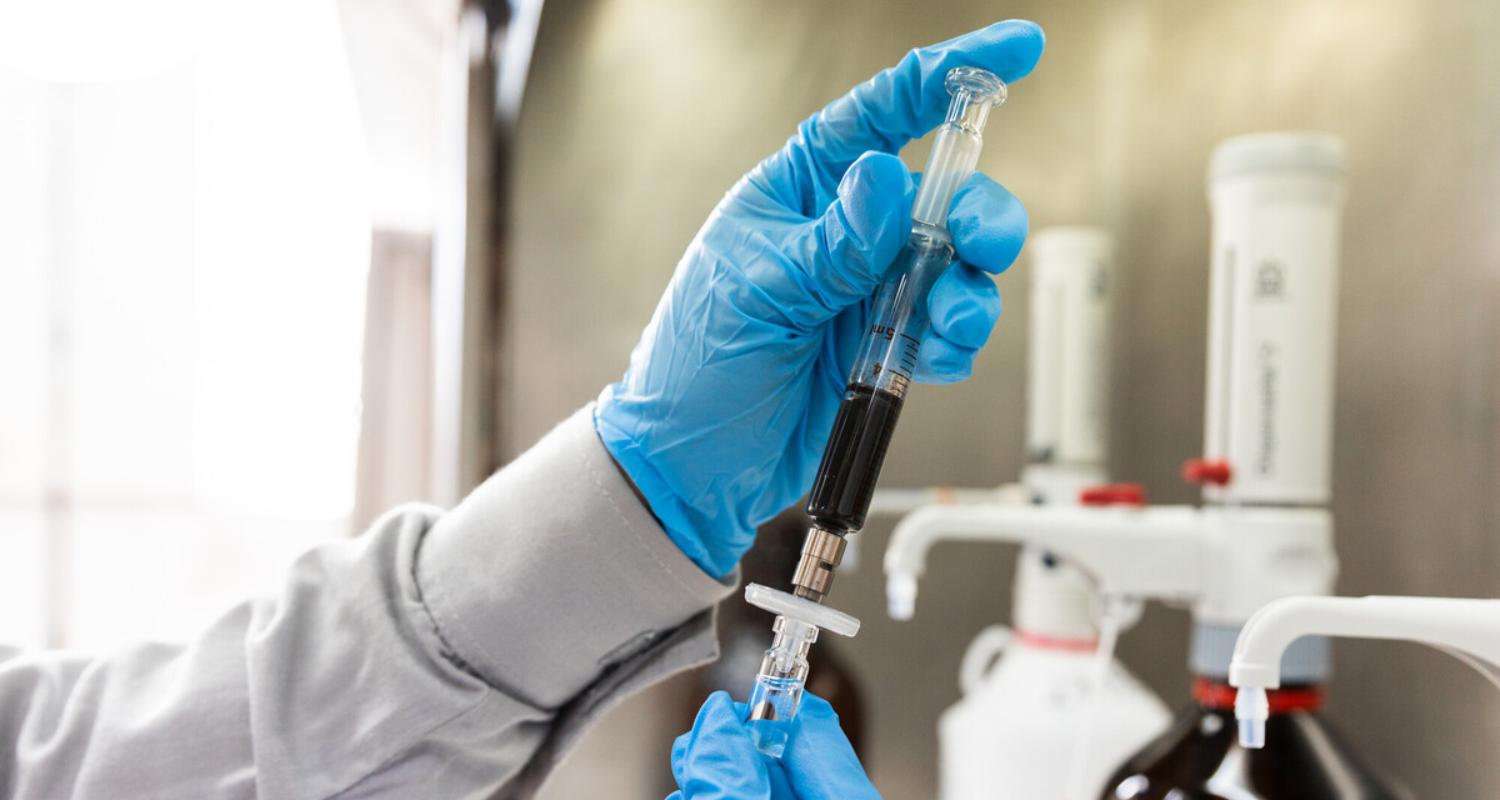 Hands with blue gloves handling a syringe with liquid inside