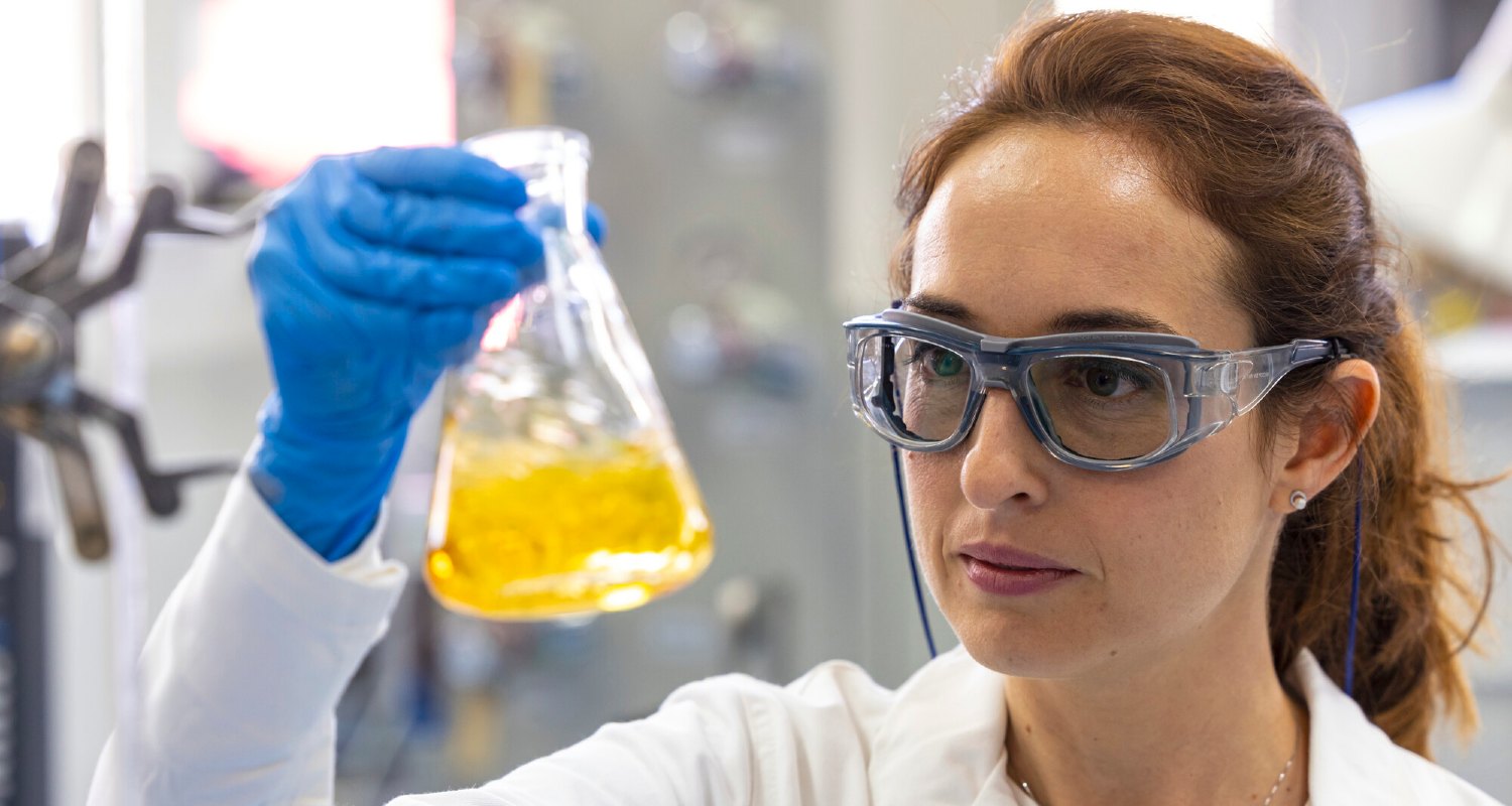 Una investigadora observa un matraz con un líquido amarillo