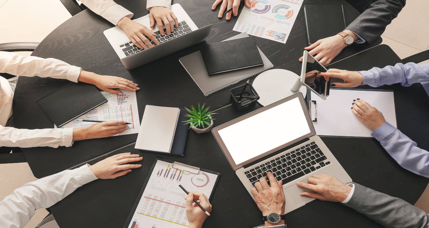 Manos encima de una mesa de trabajo con portátiles y cuadernos