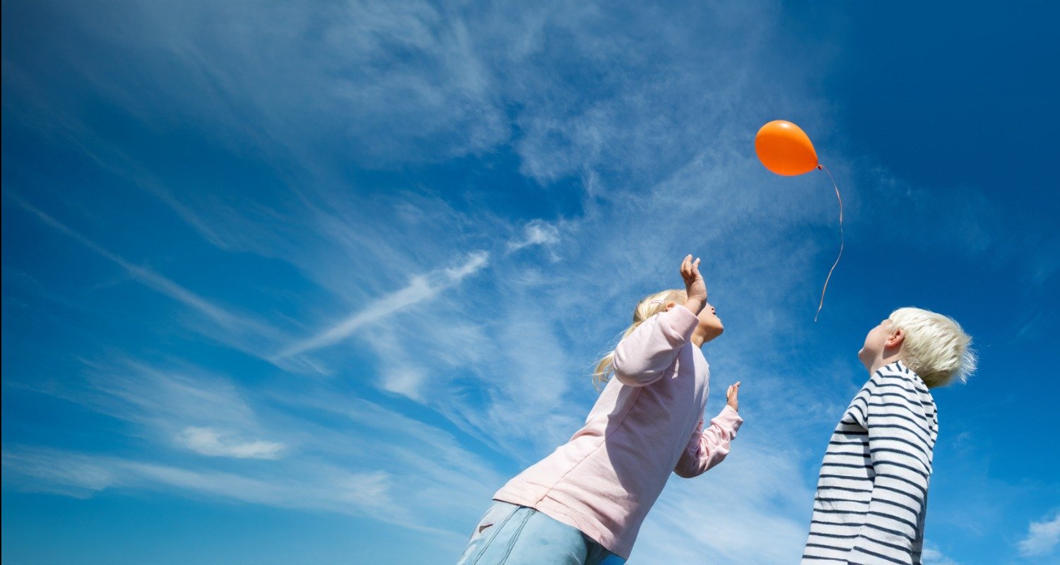 Two children looking at a balloon as it goes into the sky