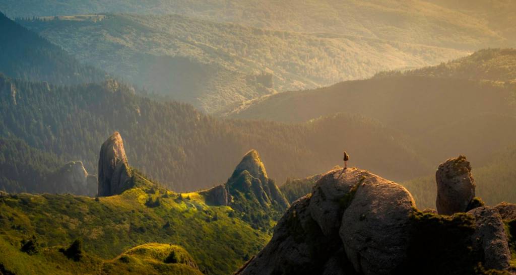 Vista de una silueta de una persona en la punta de un montaña iluminada por el sol