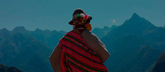 Looking at the back of a person dressed in indigenous clothing looking at a mountainous landscape at sunset