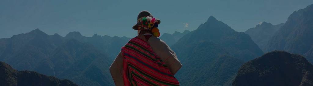 Looking at the back of a person dressed in indigenous clothing looking at a mountainous landscape at sunset